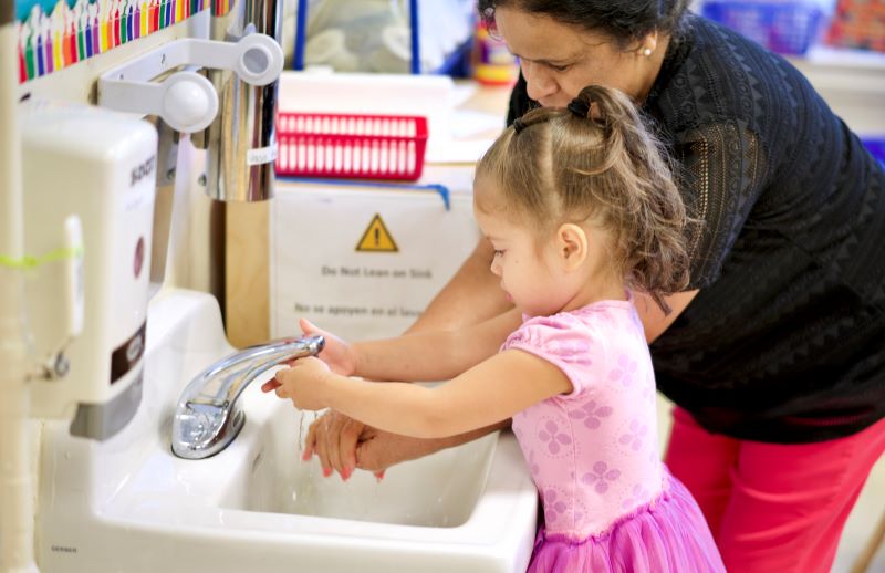 Adult helping child wash their hands at the sink.