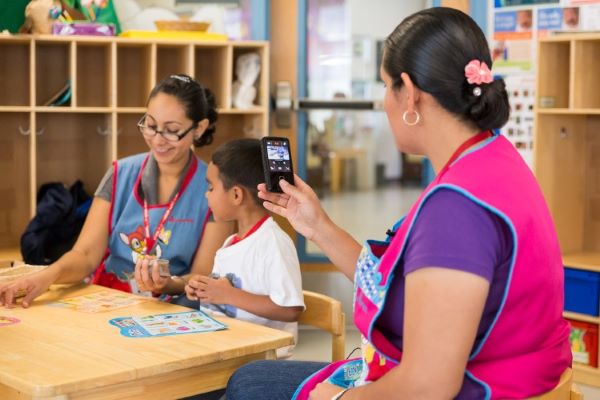 Adult using a camera to take a photo of a child and caregiver working on a class project.