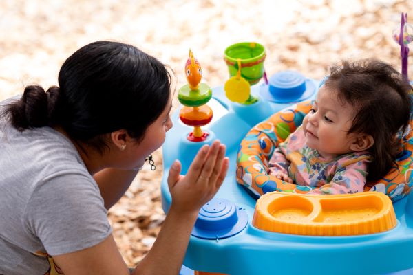 Adult clapping and interacting with infant in walker.