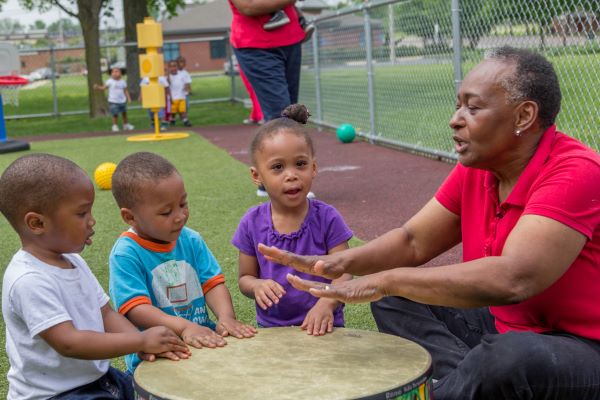 Adult and children playing a large drum.