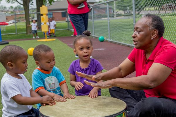 Teacher with three children all playing on a large drum.