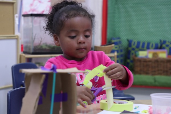 A young girl cutting off a piece of masking tape for use on an art project