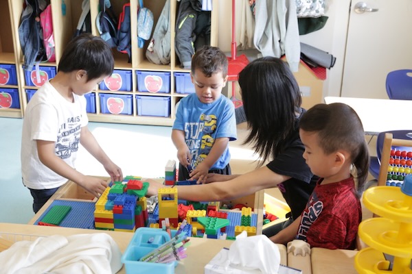 Several children reaching into a plastic tub for blocks.