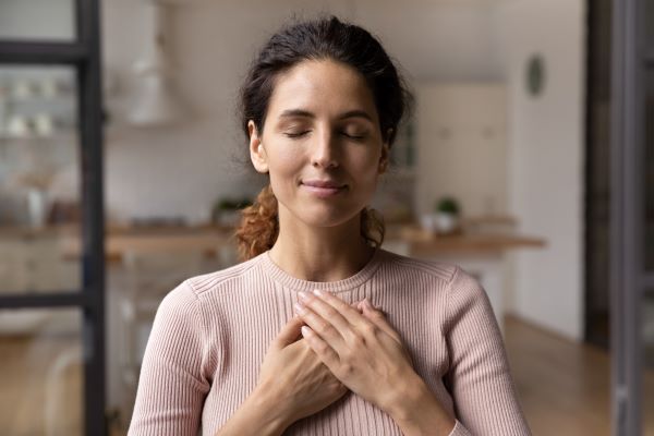 Woman with eyes closed and hands crossed over her heart.